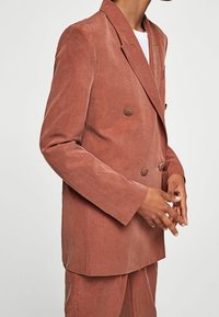 Blazer doppiopetto in rosa polveroso, realizzato in tessuto testurizzato. Presenta due bottoni rotondi, ampi rever e una vestibilità su misura.