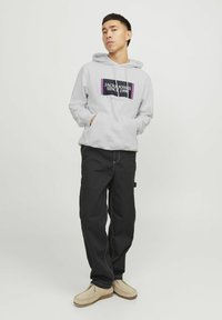 Grijze hoodie met een grafisch logo, zwarte cargobroek en beige schoenen. Bevat een aantrekbare capuchon en zijzakken. Eenvoudig ontwerp.