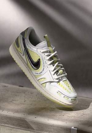 Biało-żółty sneaker Nike z czarnym logo, białymi sznurowadłami, teksturowaną podeszwą, ustawiony pod kątem na szarej betonowej powierzchni.