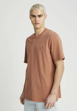 T-shirt à manches courtes de couleur rouille en coton, avec un petit logo brodé sur la poitrine gauche et un col rond.