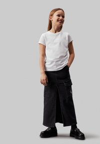 Witte t-shirt met korte mouwen en een subtiele logo, gecombineerd met een zwarte denim rok met een voorkleur en twee grote zakken. Zwarte schoenen.
