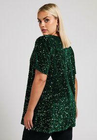 Top verde con paillettes con maniche corte, caratterizzato da una superficie testurizzata e una vestibilità ampia, completato da un colletto arrotondato e un design sul retro.