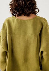 Olive zielona bluzka oversize z okrągłym dekoltem, teksturowana z lnianego materiału, z opadającymi szwami na ramionach, z delikatnym detalem w szwie na plecach.