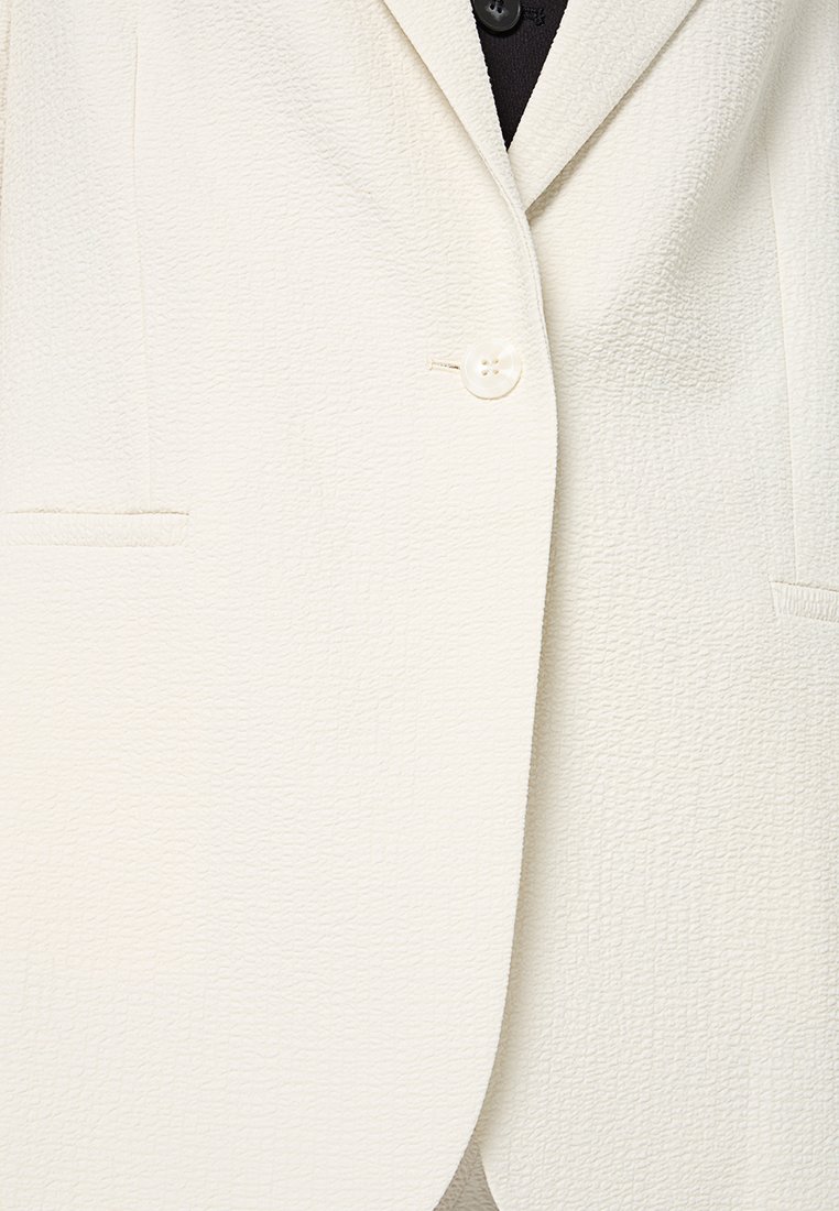 Weißer, strukturierter Blazer mit einem Ein-Knopf-Verschluss, zwei Fronttaschen und einem leicht strukturierten Design.