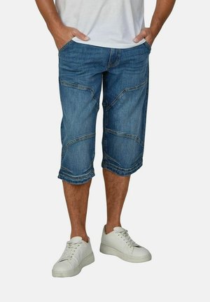 Denim capri jeans met een iets lossere pasvorm, voorzien van patchworknaden en opgerolde manchetten; gecombineerd met witte sneakers.