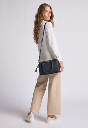 Navy leren handtas met dubbele handvatten en een afneembare schouderband. Voorzien van gouden hardware en een gestructureerde afwerking. Het model draagt beige wijde broek en sneakers.