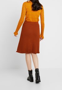 Ribbad, knälång brun kjol med volangkant, kombinerad med en strukturerad orange långärmad topp och svarta ankelstövlar.