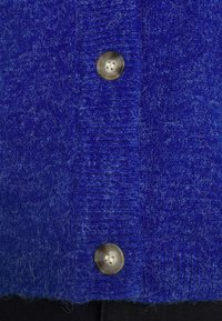 Deux boutons beige fixés sur un vêtement tricoté bleu duveteux et texturé en gros plan.