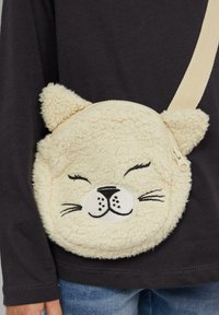 Okrąża torba w kremowym kolorze o miękkiej, pluszowej fakturze. Posiada uszy kota, haftowane oblicze z wąsami oraz zamek błyskawiczny. Regulowany pasek.