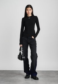 Bluză neagră cu mâneci lungi și logo alb "OFF", asociată cu pantaloni evazați din denim închis. Modelul ține o geantă mică din piele neagră cu ținte. Încălțăminte neagră.