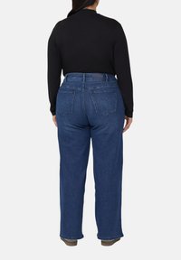 Ciemnoniebieskie dżinsy o prostych nogawkach, z pięcioma kieszeniami i gładkim pasem. Częściowo widoczna czarna bluzka z długim rękawem.