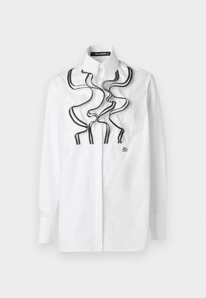 Bela srajca z gumbki, ki ima črno naborkano obrobo spredaj. Narejena je iz bombaža, ima dolge rokave in klasičen ovratnik.