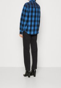 Plaid shirt in blue and black flannel, long sleeves, curved hem, buttoned cuffs; paired with black jeans and heeled ankle boots.