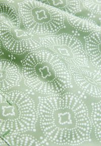 Zöld és fehér kör alakú mintákkal díszített textil, pöttyös elemekkel; sima felület, finom fényesség és redőzött megjelenés.
