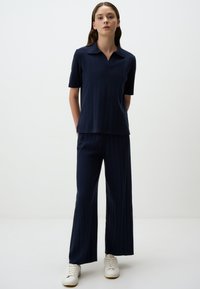 Marineblauw geribbelde knit set bestaande uit een polo met korte mouwen en wijde broekspijpen. De stof heeft een soepele textuur; beide stukken hebben een comfortabele pasvorm.