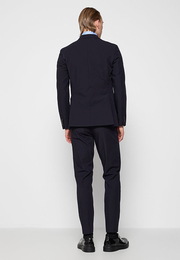 Marineblaue Sakkos mit schmaler Passform und Revers, kombiniert mit passenden, taillierten Hosen und schwarzen Lederschuhen, zeichnen sich durch klare Linien und minimalistische Details aus.