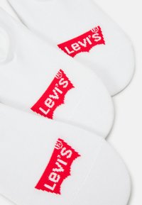 Meias brancas de tornozelo com um proeminente logótipo vermelho da Levi's num design clássico. Feitas de um material suave com uma textura lisa.