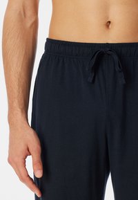 Navy blue cotton joggers with an elastic waistband, adjustable drawstring, and smooth texture. Close-up of hand resting near the waist.