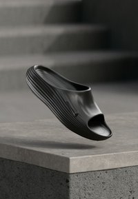 Black slide shoe with open toe, textured ribbed design, and a Nike logo accent. Made from a smooth, flexible material.