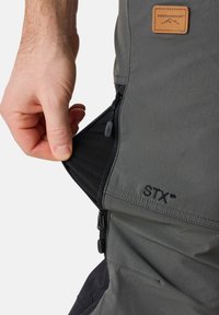 Händisches Öffnen des seitlichen Belüftungsreißverschlusses aus Netz bei grauen Swedemount STX Outdoor-Hosen.