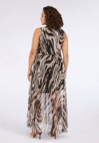 Robe fluide sans manches avec un motif animalier noir et beige, présentant une taille cintrée et un panneau arrière long et transparent.