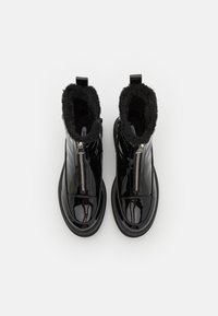 Bottines noires en vernis avec doublure en fausse fourrure et fermeture à glissière. bout arrondi et semelle épaisse, avec une finition lisse et brillante.