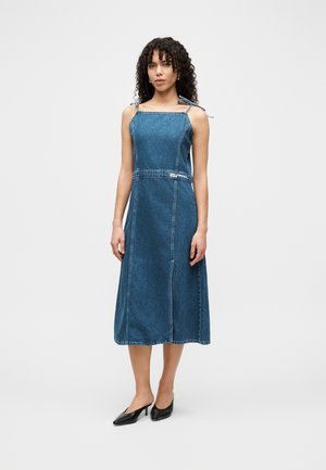 Denim dress with a fitted bodice, A-line skirt, and adjustable tie straps. Mid-length, in a medium blue wash with visible stitching details.
