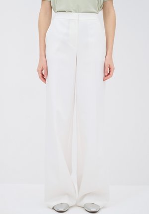 Personne portant un pantalon blanc taille haute à jambes larges, associé à des chaussures pointues argentées métalliques et un haut vert clair rentré.