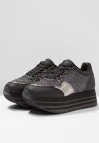 Mustat alustan lenkkitossut, joissa on kiiltävä musta ja kimalteleva tumma tekstiilipinta, mustat nauhat ja teksturoitu pohja pitoa varten.