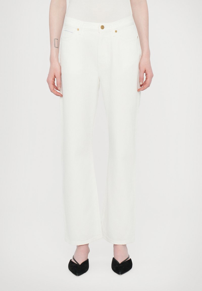 Jeans blancs à jambes larges en tissu mélangé coton, avec une fermeture à bouton doré, cinq poches et un léger effet délavé. Associés à des chaussures noires.