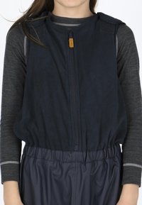 Marine fleecevest med lynlås og skulderlapper, parret med en mørkegrå langærmet top med kontrasterende syninger.