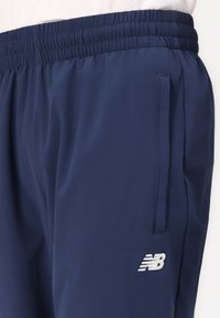 Navyblauwe sportbroek met elastische tailleband, zijzak en wit New Balance-logo. Gemaakt van lichtgewicht, glad materiaal.