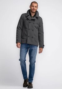 Anthrazitgrauer doppelseitiger Peacoat mit breitem Kragen, Knopfdetails und weicher Textur, kombiniert mit blauen Jeans und braunen Stiefeln.