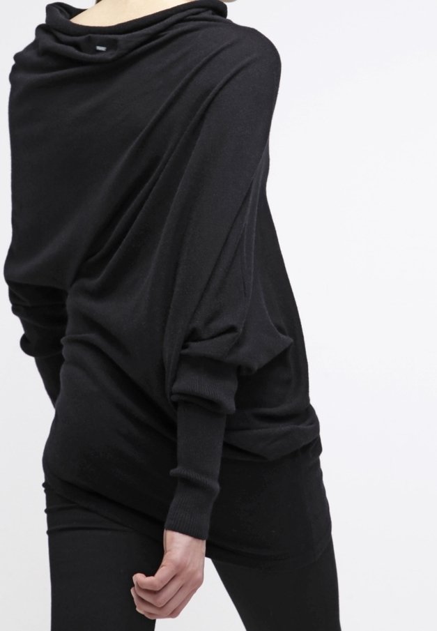 Femme portant un haut noir à manches longues ample avec un col drapé et des poignets ajustés, assorti à un pantalon noir.