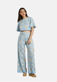 Hellblaues Baumwoll-Zweiteiler-Set mit einem Cropped-Top mit geprägten Mustern und weiten Hosen mit passendem Gürtel.