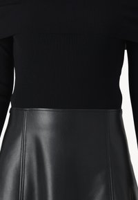 Top a maniche lunghe a coste nere abbinato a una gonna di pelle nera. La gonna presenta una texture liscia e cuciture visibili lungo le giunture.