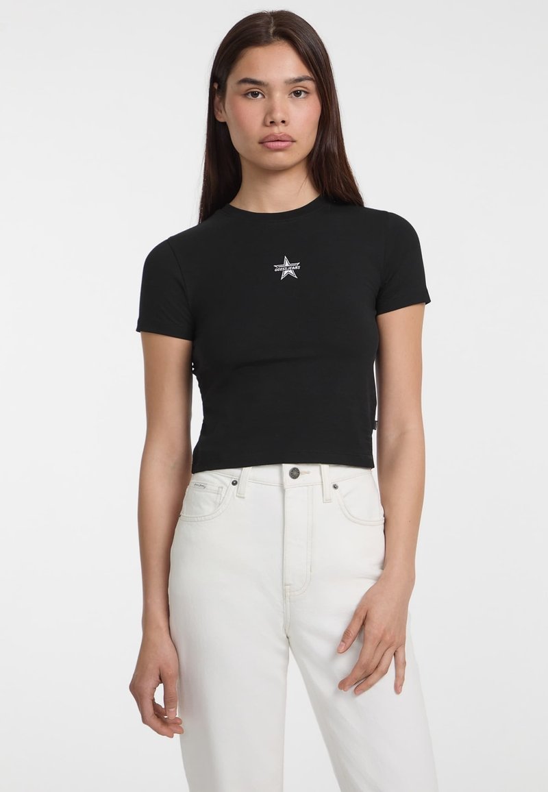 Musthave musta lühikeste varrukatega lühike t-särk ümmarguse kaelusega ja hõbedase tähegraafikaga rinnal, kombineeritud kõrge vöökohaga valgete teksadega.