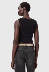 Czarny bezrękawnik z okrągłym dekoltem, zestawiony z wysokimi dżinsami w ciemnym kolorze oraz metalową paskiem o teksturowanej powierzchni.