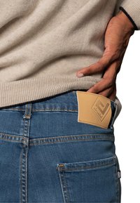Jeans de mezclilla en azul con un parche de cuero marrón en el bolsillo trasero. La tela parece resistente, con detalles de costura visibles.