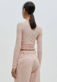 Langärmliges, geripptes rosa Oberteil mit einem cropped Design, kombiniert mit hoch taillierten hellrosa Hosen mit Gesäßtaschen.