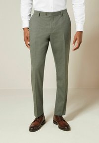 Light green, tailored trousers with a smooth texture, front creases, and a single button closure, paired with brown dress shoes.