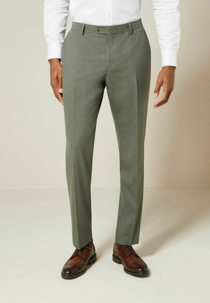 Pantalones de corte recto en verde claro, con una textura suave, pliegues en la parte delantera y un cierre de botón único, combinados con zapatos de vestir marrones.