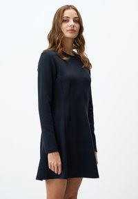 Robe à manches longues de couleur bleu marine, fabriquée en tissu doux. Présente une coupe décontractée avec un léger évasement à l'ourlet et des détails de couture minimalistes.