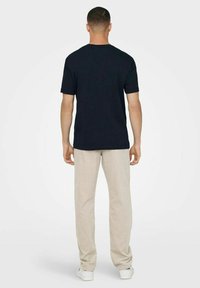 Schwarzes Kurzarm-T-Shirt mit Rundhalsausschnitt, kombiniert mit beigen Cordhosen. Der Stoff wirkt glatt und hat ein einfaches, klassisches Design.