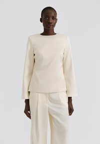 Kremfarget topp med lange ermer, rund hals og glatt tekstur, kombinert med matchende lyse bukser. Enkel, moderne design.