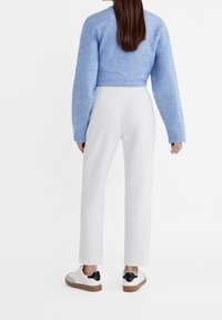 Maglione corto celeste con polsini a costine abbinato a pantaloni bianchi. Modella che indossa sneakers bianche con dettagli neri e suola beige.