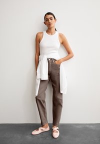 White ribbed sleeveless top, brown high-waisted pants, and light pink flats with cut-out details. Outfit details include a tied white shirt.