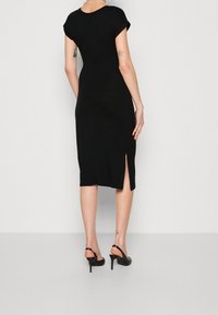 Černé přiléhavé šaty s krátkými ohrnutými rukávy, do kolen, s bočním rozparkem. Hladká textura a minimální design. Černé slingback podpatky.