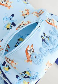 Kék erszény narancssárga és kék rajzfilmszerű kutya mintákkal, texturált „bluey” díszítéssel. Cipzáras záródás kerek húzófüllel.