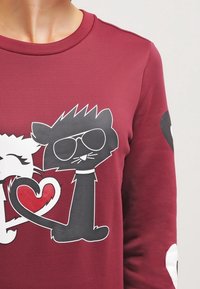 Bordowy długi rękaw sweatshirt z graficznym wzorem przedstawiającym dwa rysunkowe koty, jeden czarny w okularach przeciwsłonecznych, trzymający czerwony kształt serca.